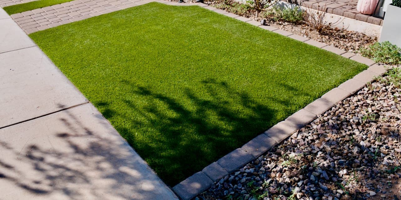 A rectangle of artificial turf edged by pavers on one side and gravel on the other.